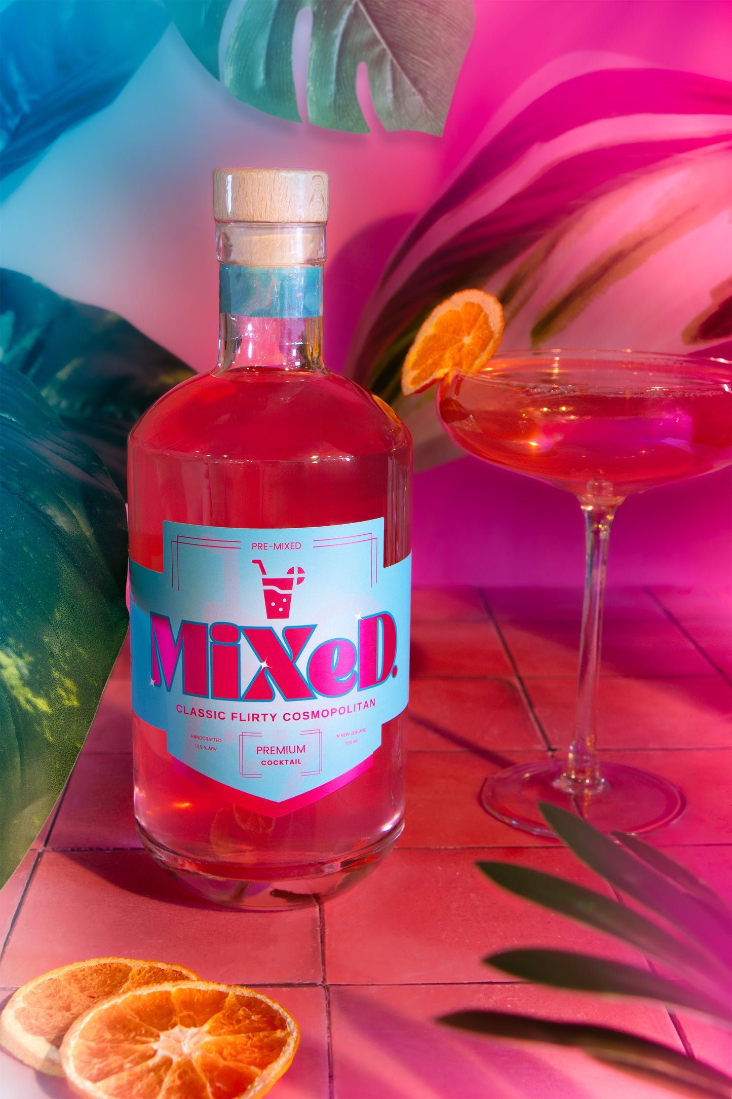 Bottle of 'MIXED' cosmopolitan cocktail with a glass and orange slices on a colourful background