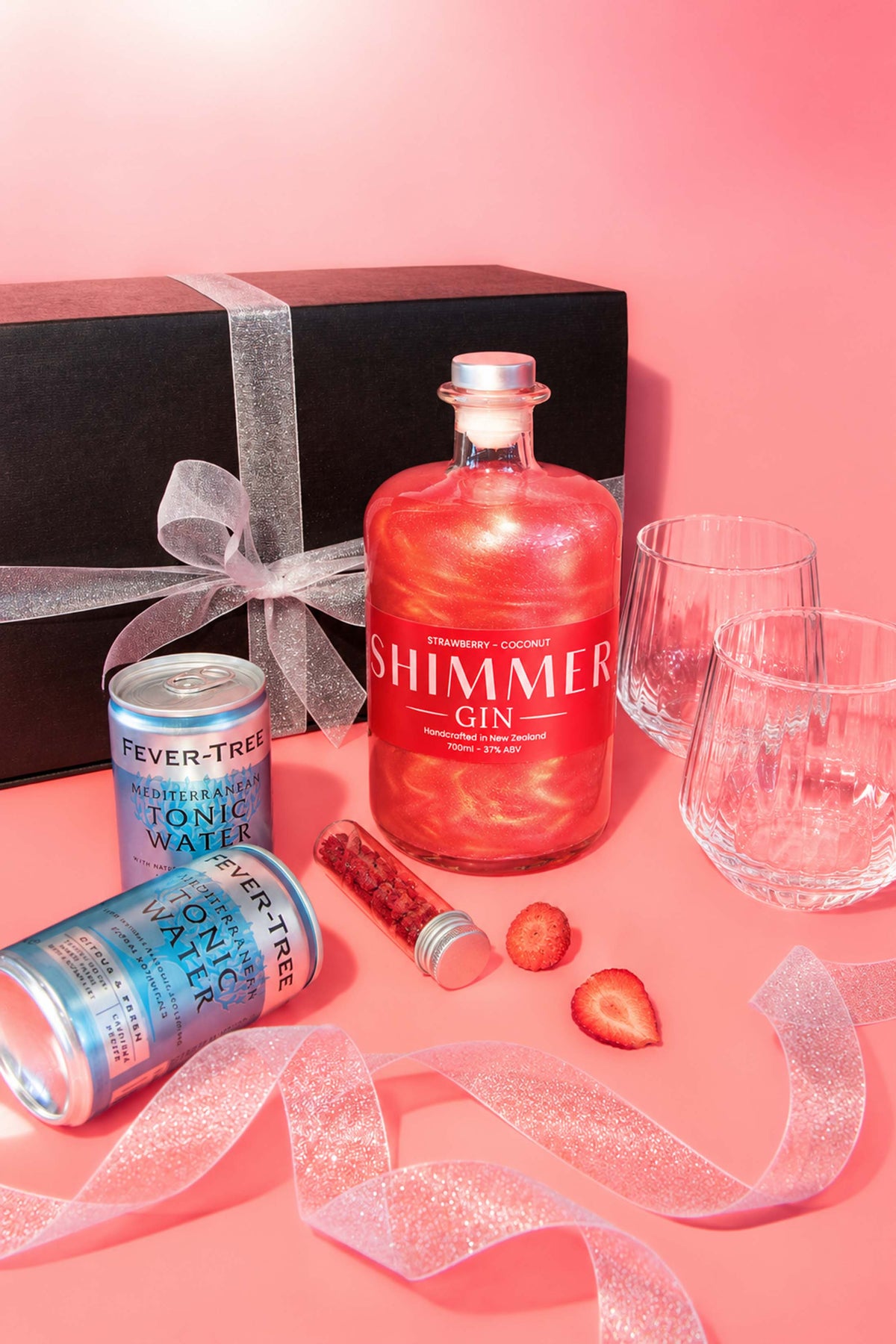 SIP Distilling Co. Red Shimmer Gin Gift Box with strawberry and coconut gin, tonic water, glasses and gift packaging on a pink background.