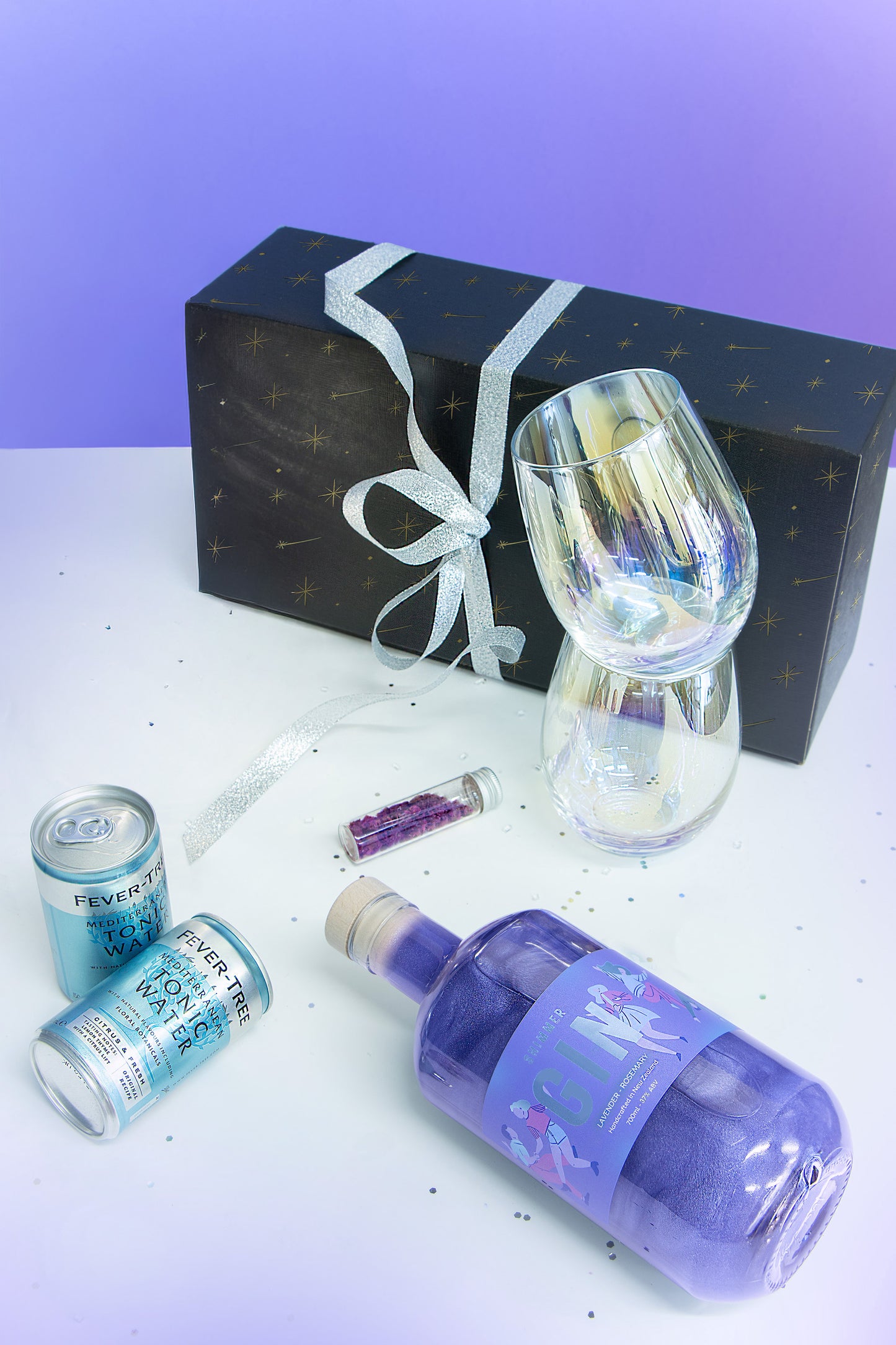 Alcohol gift set with bottles, cans, and a glass on a white surface with a purple background.