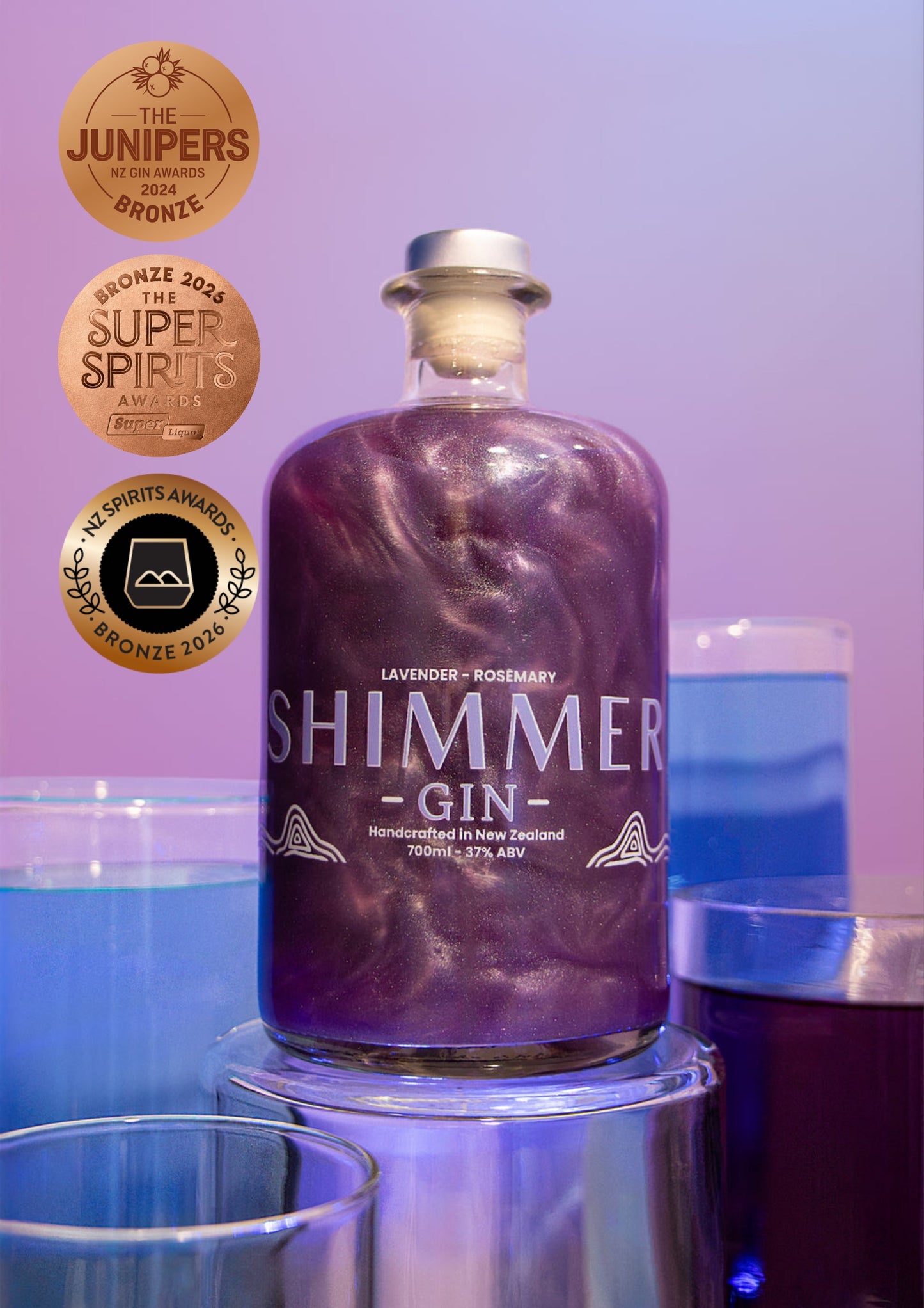 A bottle of Shimmer Gin lavender-rosemary flavored liquefied gin, shown on a metallic pedestal with blue and purple cocktails in the background and award badges on the left.