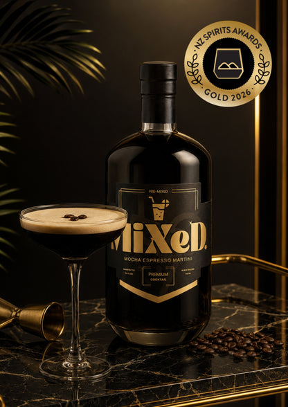 A bottle of Mixed Moscow Mule cocktail spirit with a gold and black label, displayed next to a prepared cocktail in a coupe glass on a marble tray, with coffee beans and a gold award badge.