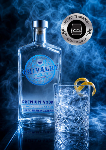A bottle of Chivalry Premium Vodka stands beside a clear glass filled with ice and a curled lemon twist, set against a smoky blue background. A round award badge for the 2026 Spirits Awards is visible in the upper right.