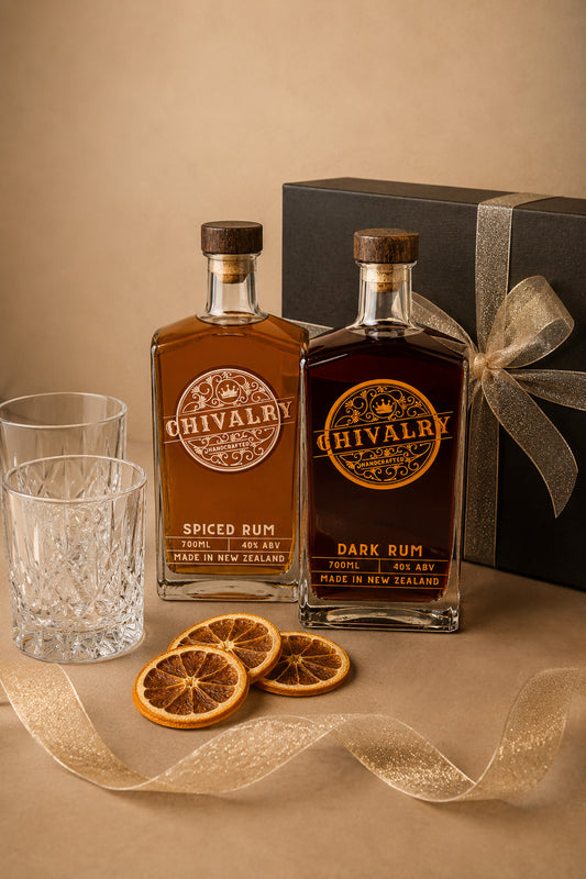 Two bottles of Chivalry rum with a gift box, glasses, and orange slices on a beige surface.