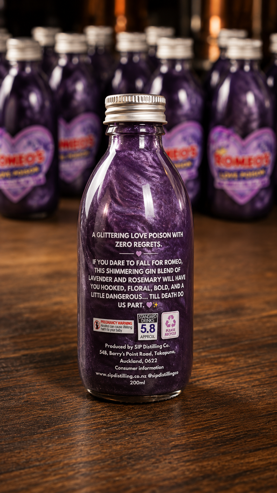 A purple glass bottle of Romeo's Grape Alcoholic Gin with a silver cap, standing on a wooden table with other matching bottles blurred in the background.