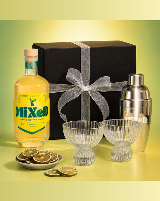 Cocktail set with 'Mixed' bottle, shaker, and glasses on a yellow background