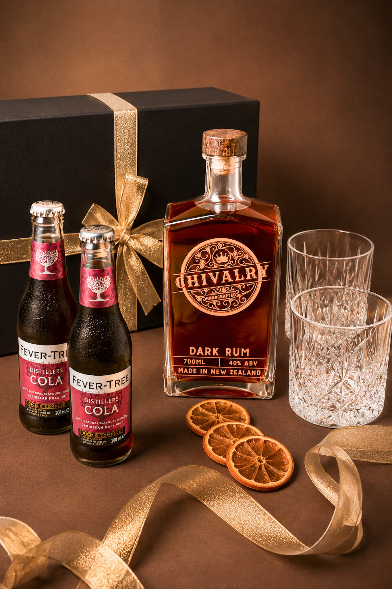 Chivalry Dark Rum bottle with Fever-Tree Cola bottles and glasses on a brown surface.