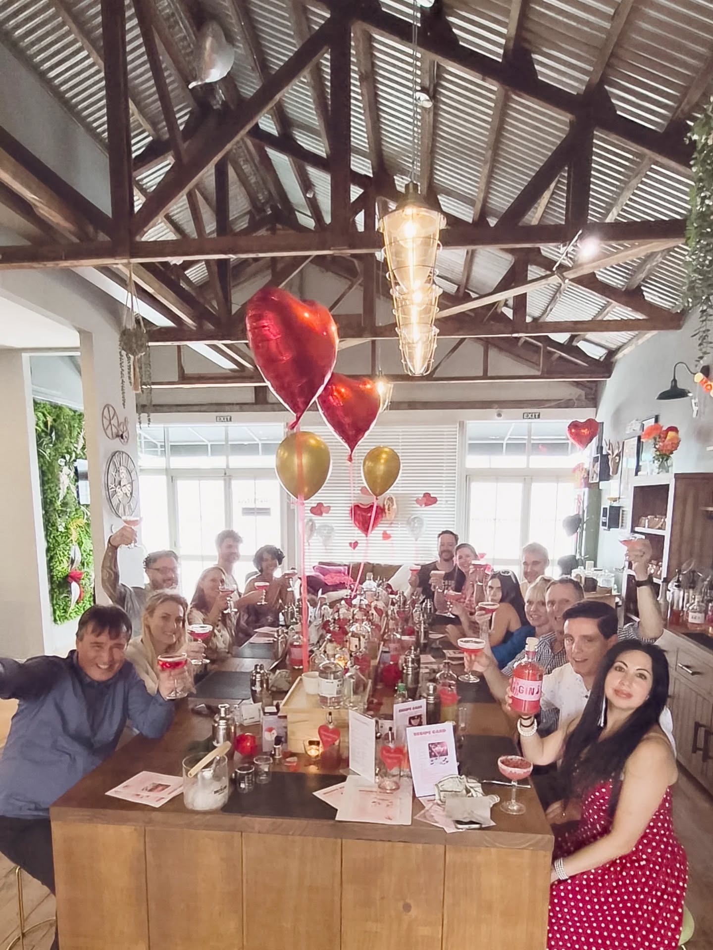 Group of people celebrating at a table with drinks and decorations in a modern indoor setting.