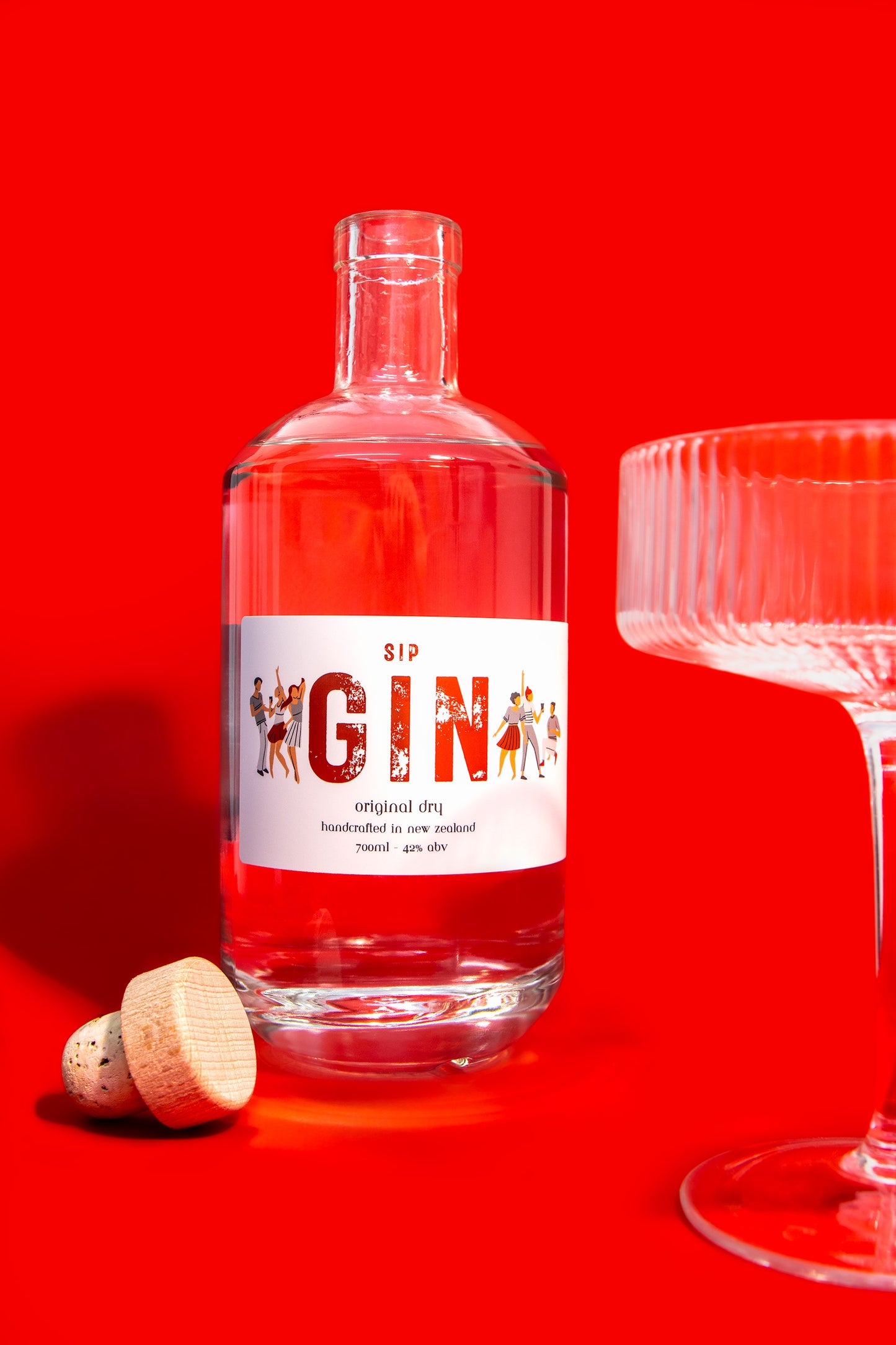 Bottle of gin with a red label on a red background, next to a glass and cork.