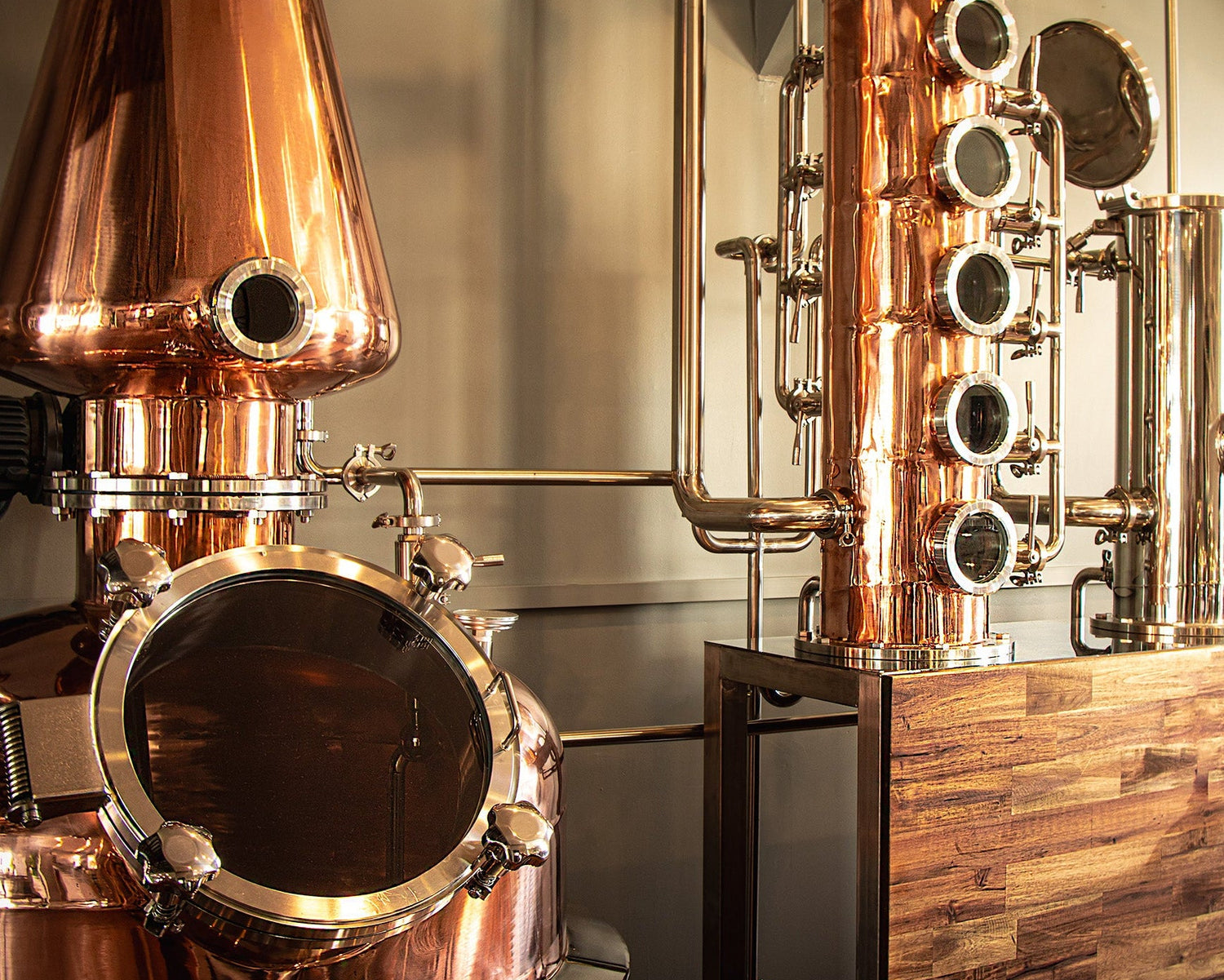 Copper pot stills and tall column stills inside SIP Distilling’s production area, featuring polished metal and wooden panel detailing.