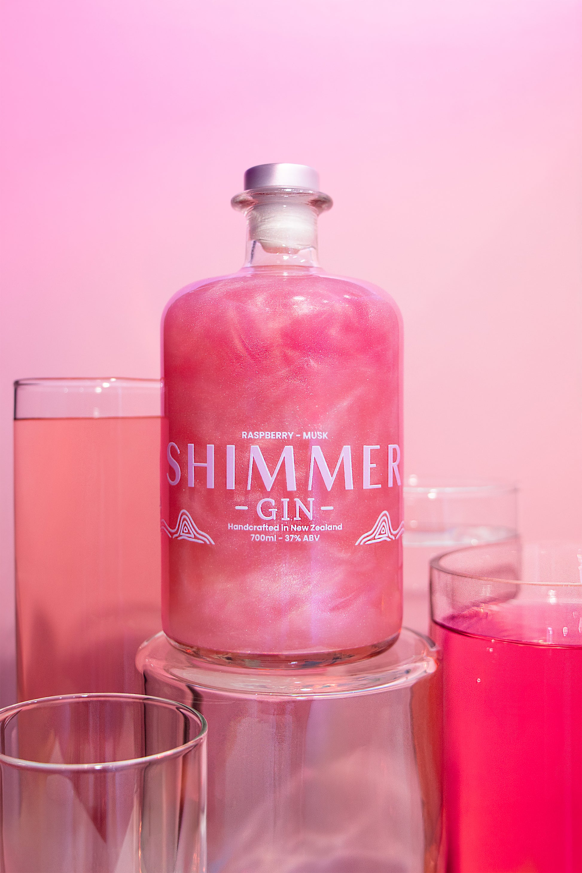 Shimmer gin bottle with pink liquid and glasses on a pink background
