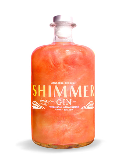 A clear glass bottle of Shimmer Gin with a white cap, filled with a vibrant orange-pink liquid. The label features the brand name 'SHIMMER' in large gold letters, with 'GIN' written below in white, and 'MANDARIN - RED BUSH' at the top.