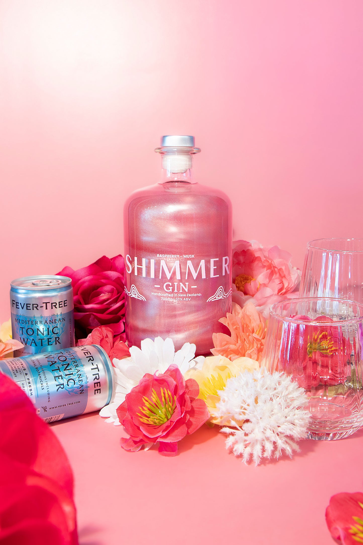 Shimmer gin bottle with flowers and cans on a pink background
