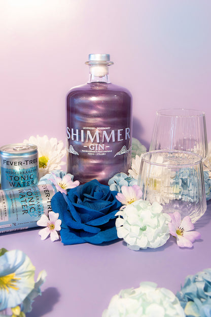 Shimmer gin bottle with tonic water cans and flowers on a purple background