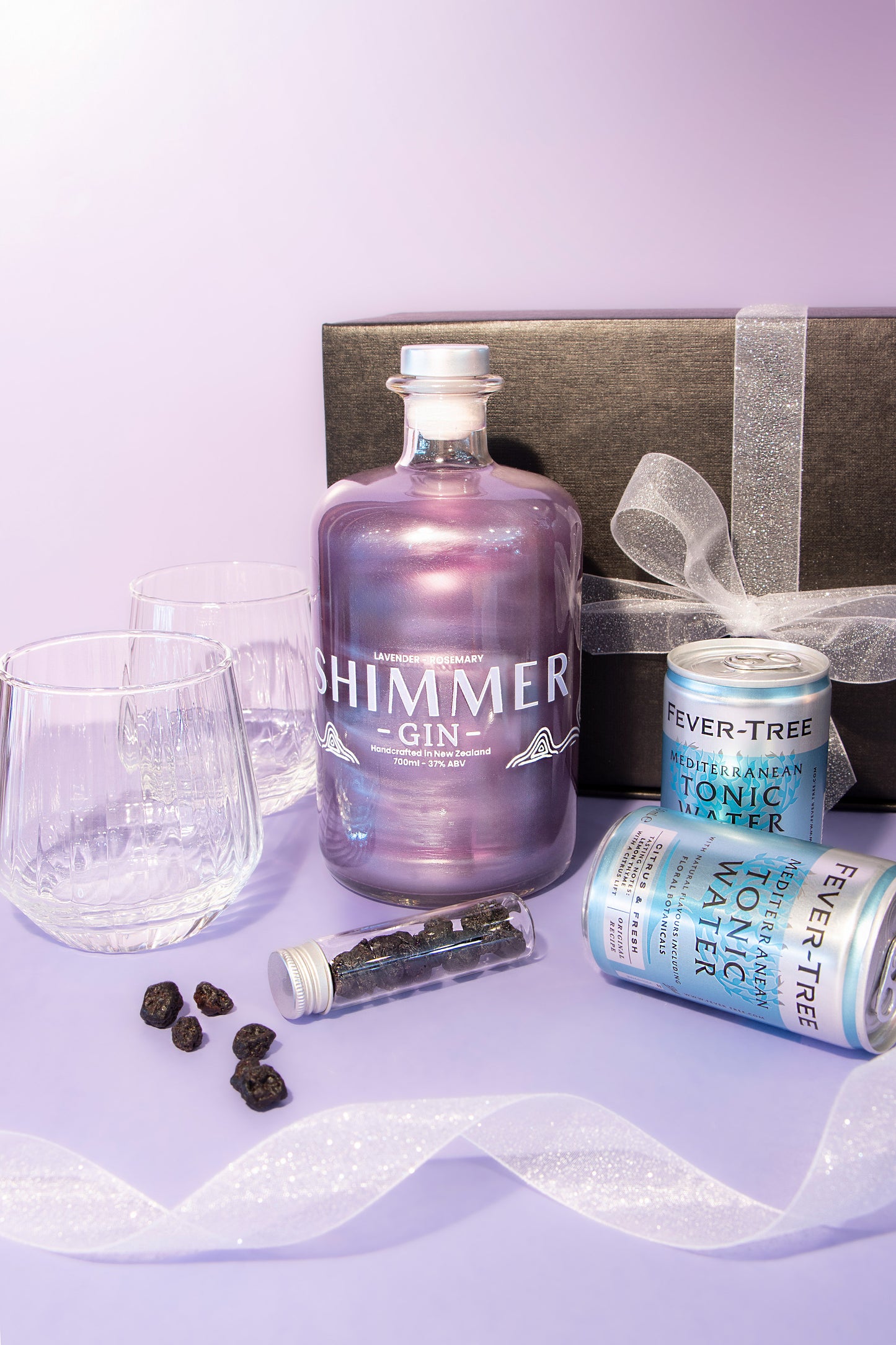 Bottle of Shimmer gin with tonic water and glasses on a purple background