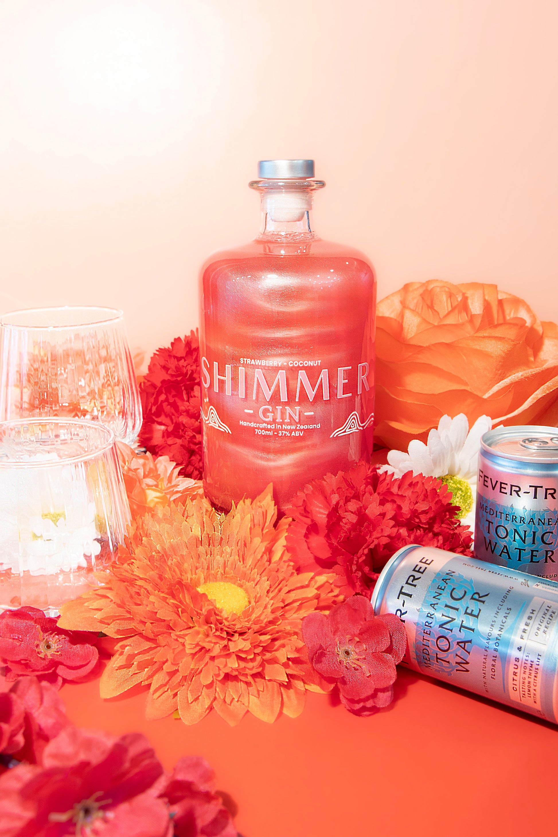 Shimmer gin bottle with flowers and tonic water on a pink background