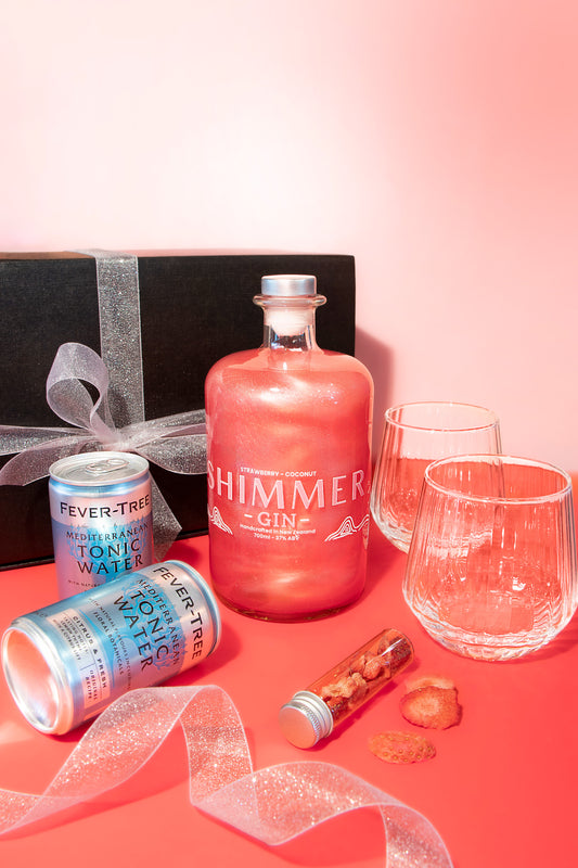 Himmer Gin bottle with tonic water cans, glasses, and a gift box on a pink background