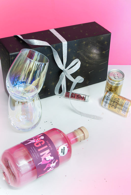 Bottle of pink gin with a glass, gift box, and can on a white surface with pink gradient background