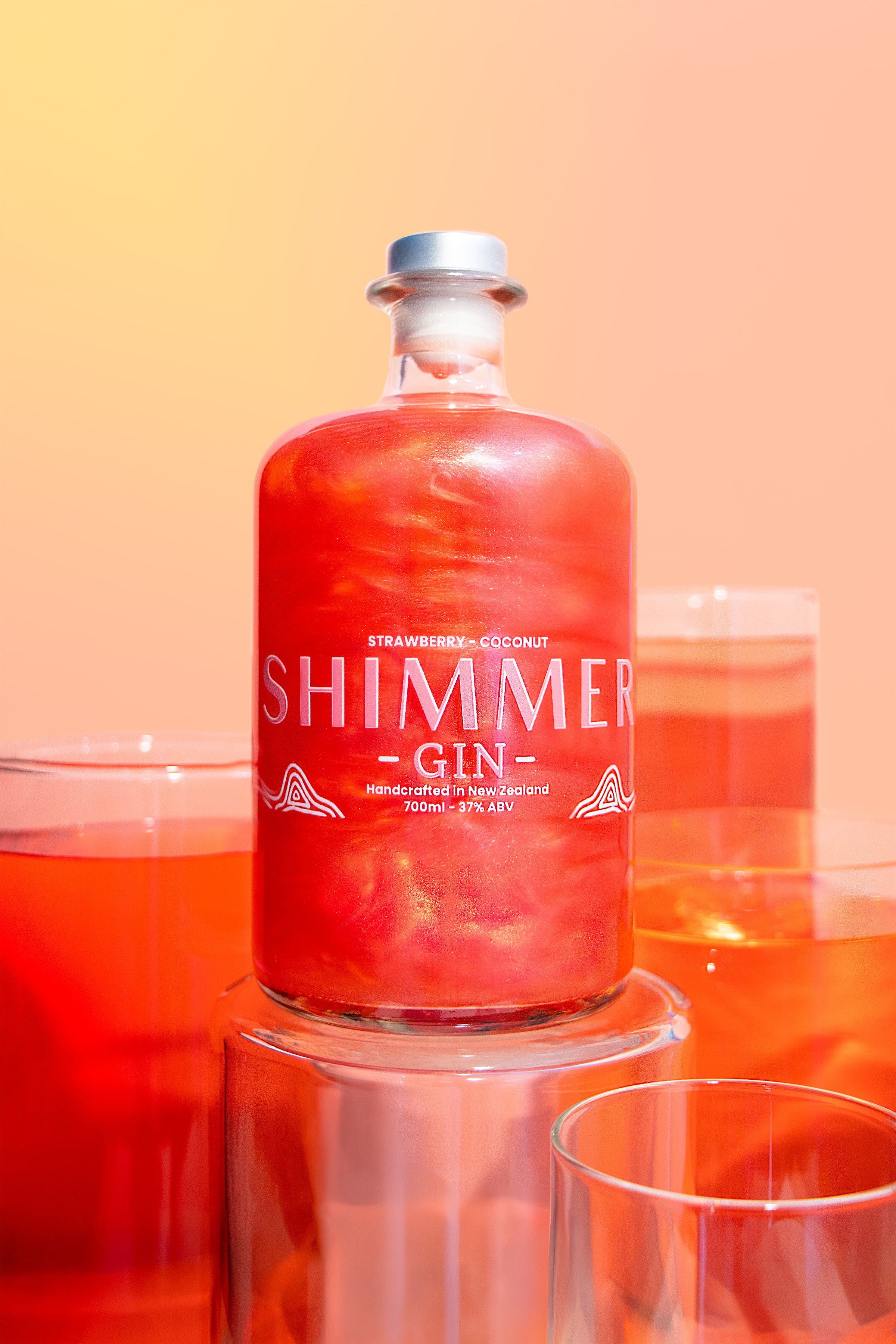 Bottle of Shimmer Gin with a red liquid on a peach background