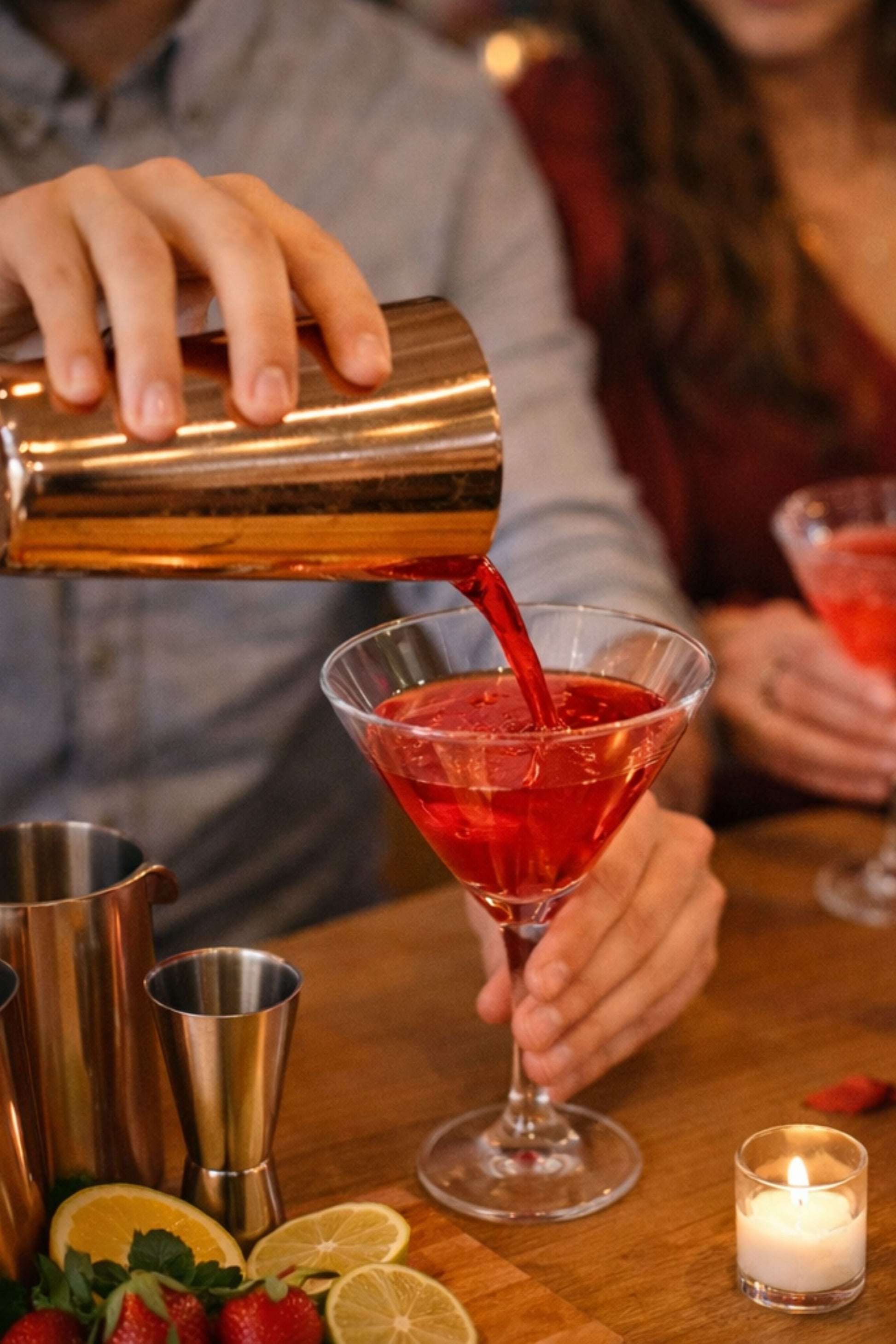 Person pouring a red cocktail into a glass with a blurred background
